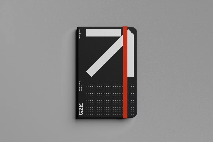 A black notebook with a bold white graphic and red elastic band resting on a neutral grey background.