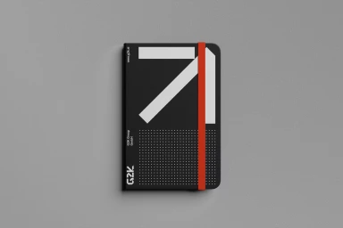 A black notebook with a bold white graphic and red elastic band resting on a neutral grey background.