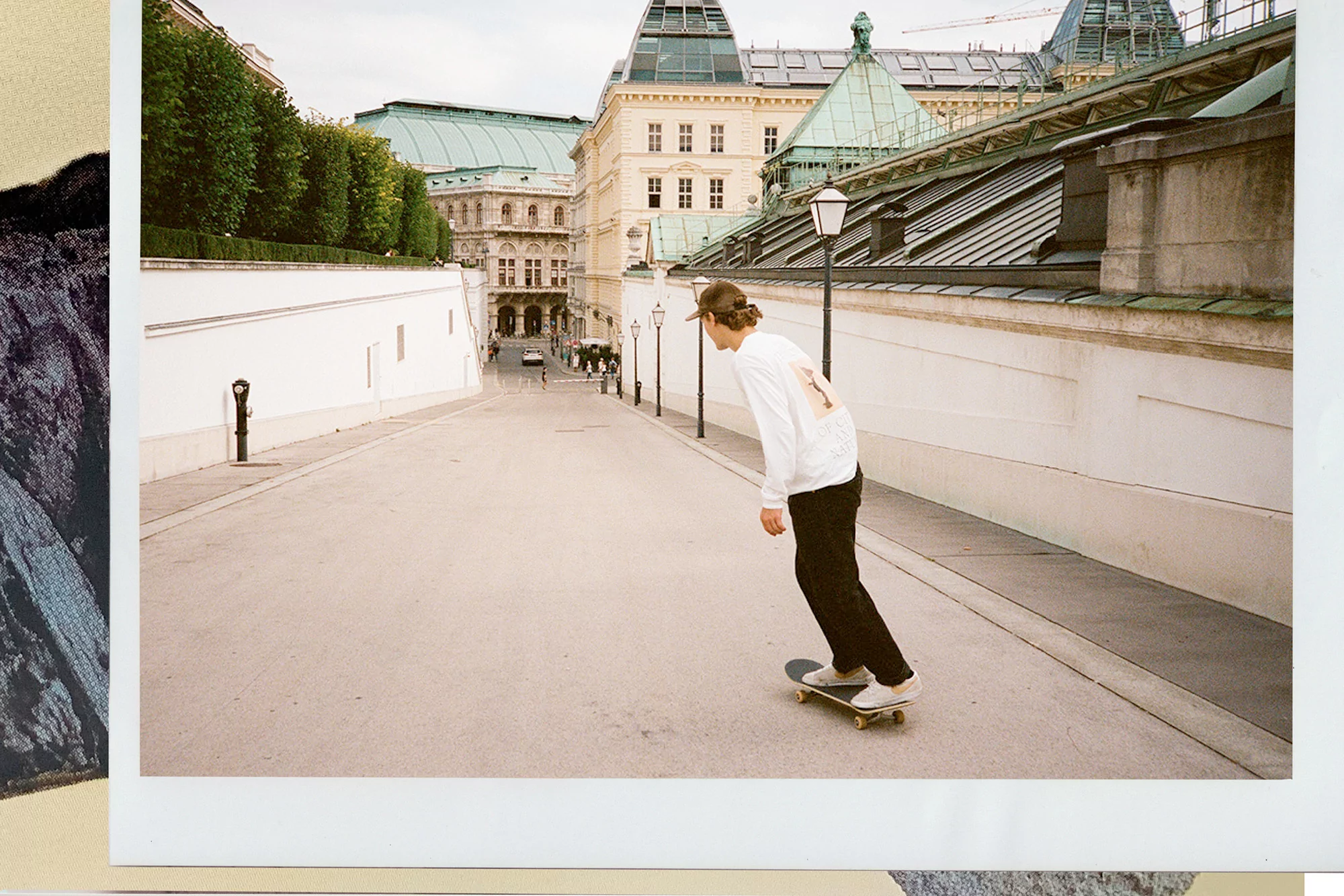 A person rides a skateboard on an urban street with European architecture in the background, capturing a moment of city life and recreation.