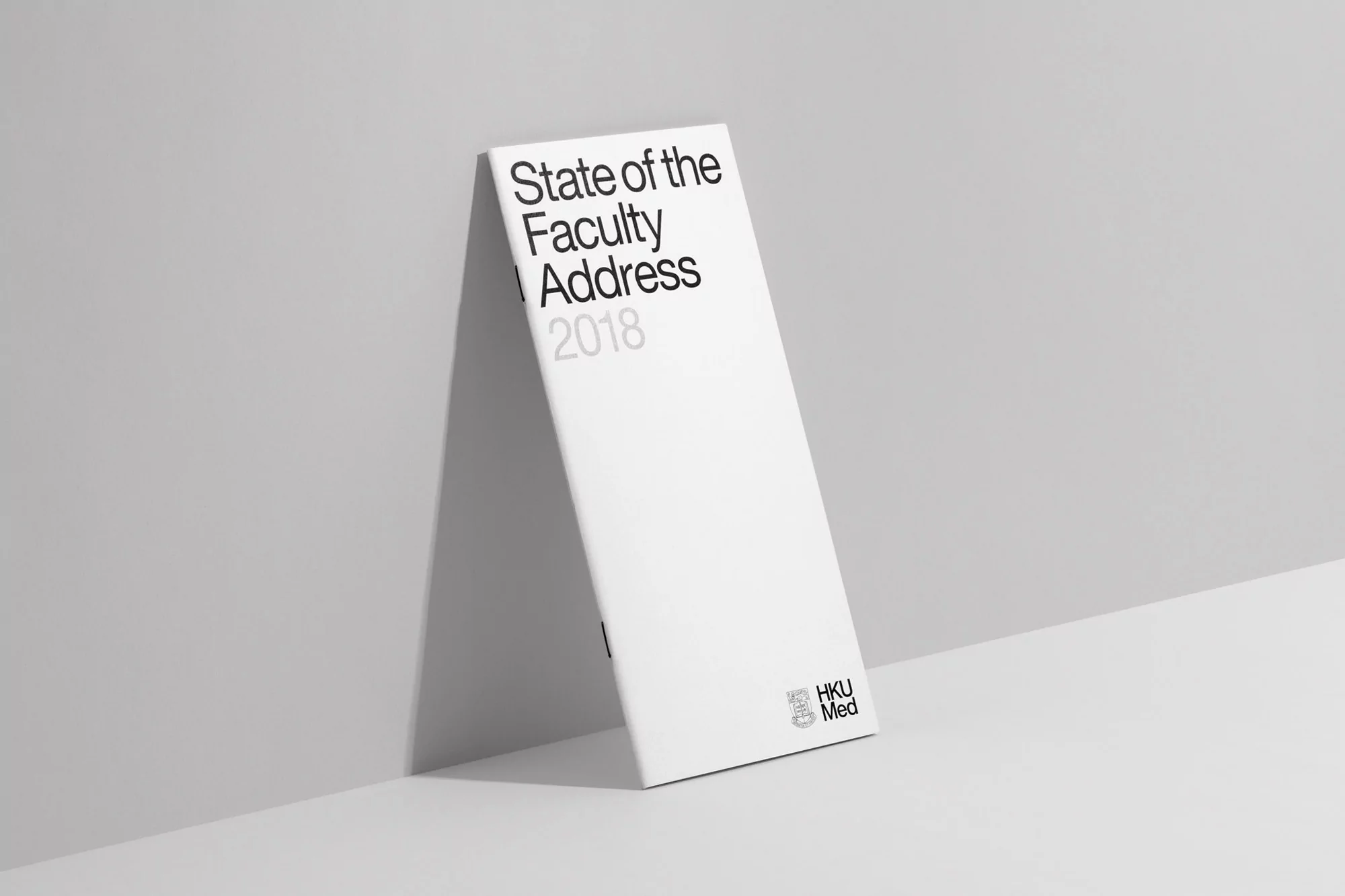 White book titled 'State of the Faculty Address 2018' stands against a grey wall, showcasing simple and modern design elements.