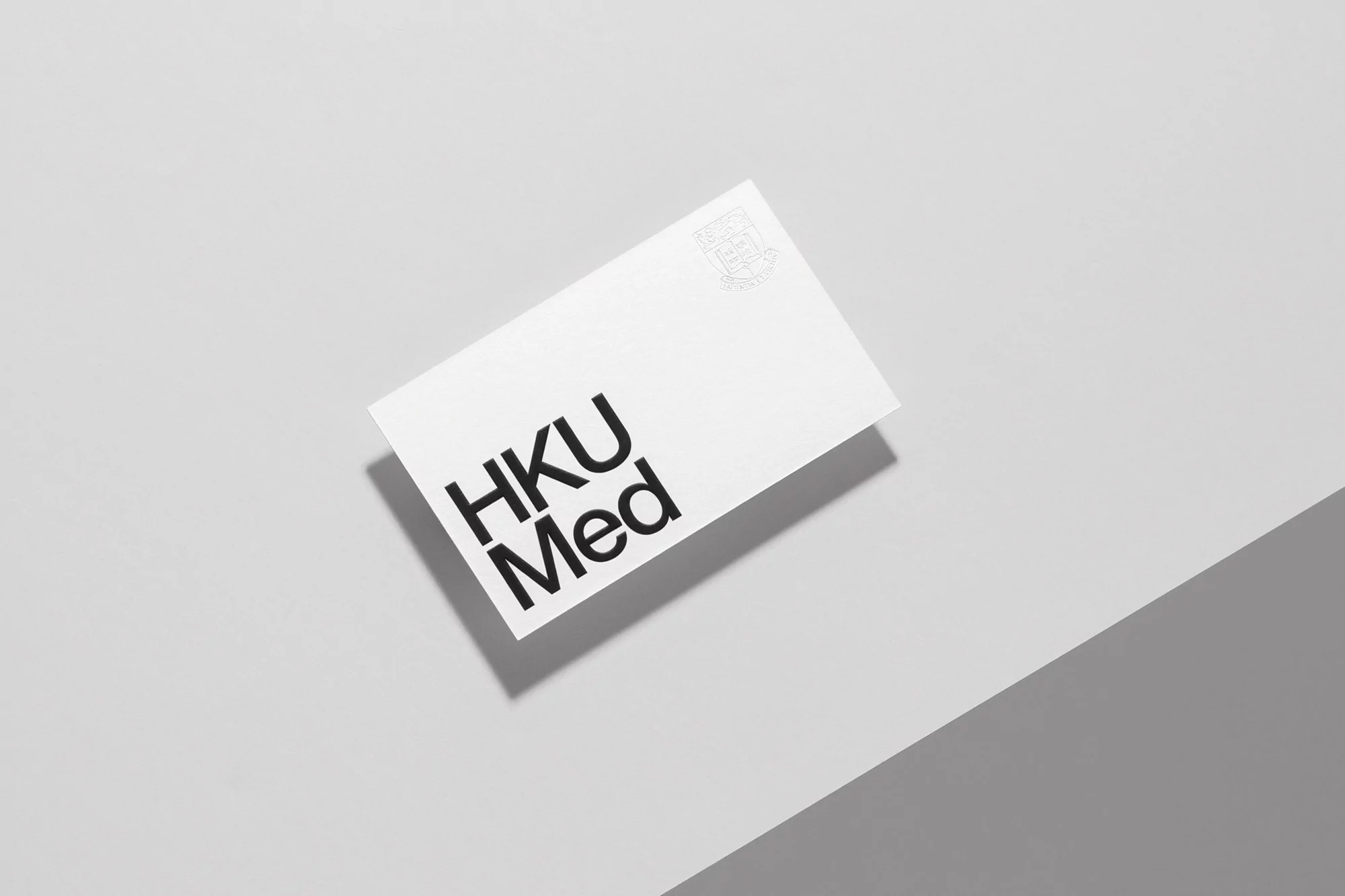 White rectangular card with 'HKU Med' in bold black text, floating on a light grey surface with a diagonal shadow creating depth.
