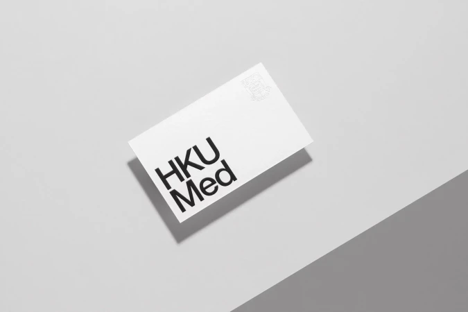 White rectangular card with 'HKU Med' in bold black text, floating on a light grey surface with a diagonal shadow creating depth.