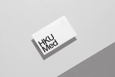 White business card featuring HKUMed typography resting on a dual-tone grey surface, captured from above.