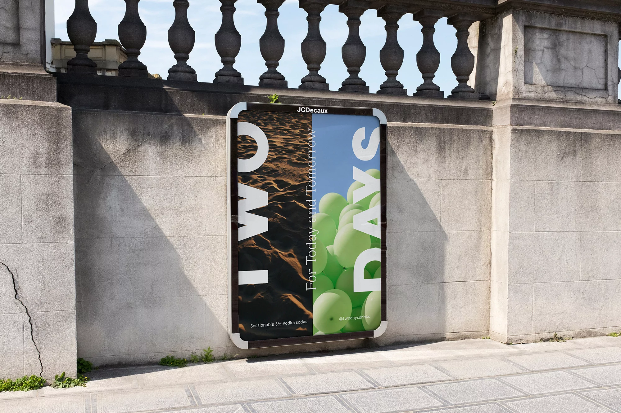 Outdoor advertising billboard on a grey stone wall displaying an ad for 'TWO DAYS,' featuring a desert scene and green balloons.