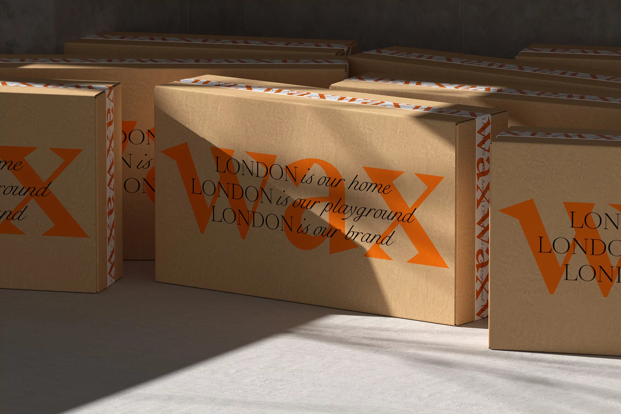 Several tan-colored shipping boxes are seen in a close-up studio shot with orange lettering, stacked in rows with shadows cast across them.