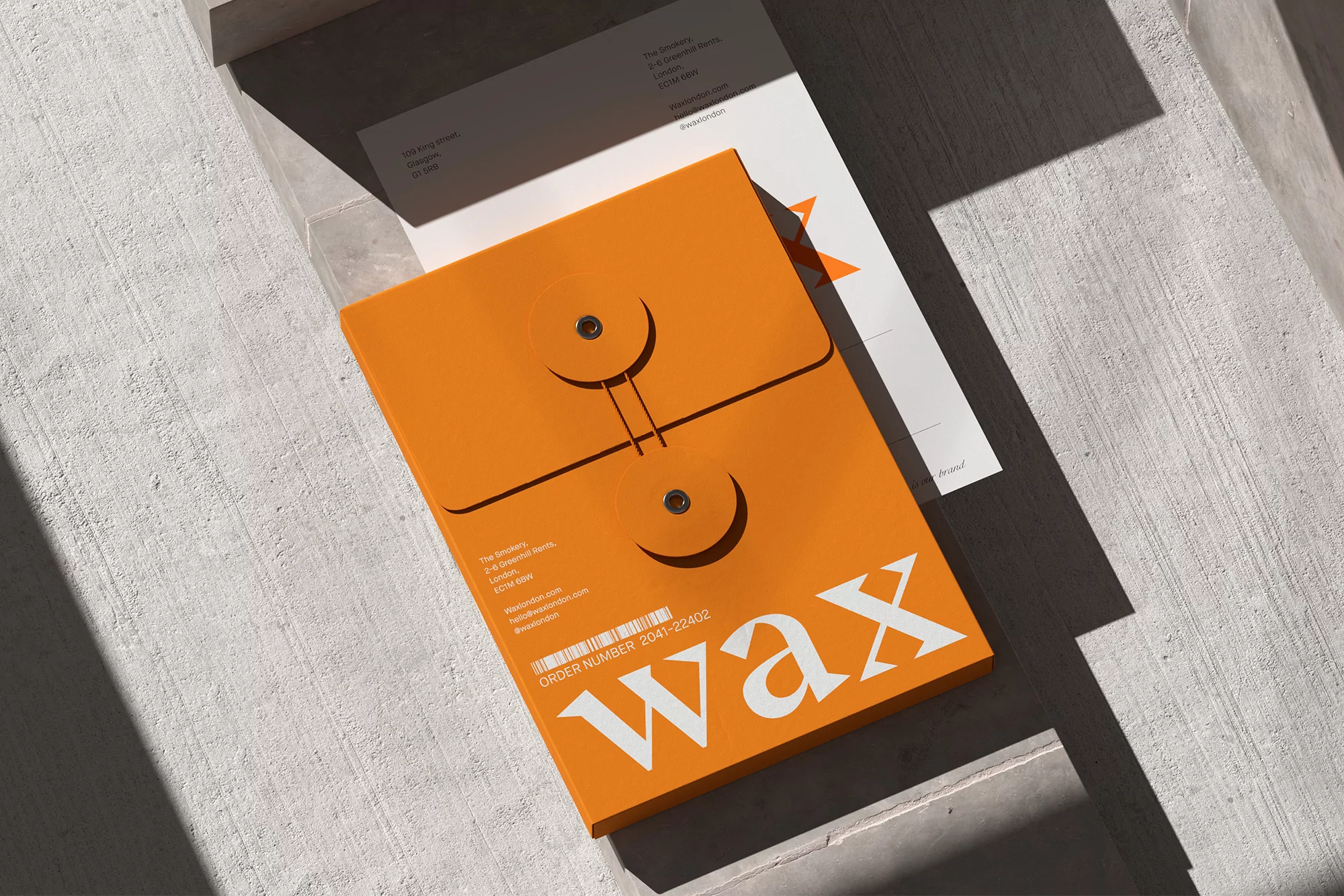Eye-level, close-up shot of a bright orange envelope with white 'wax' lettering, positioned on a textured grey surface with soft lighting.