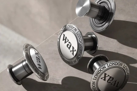 Four circular metallic hardware pieces with the Wax London brand name on a concrete surface.