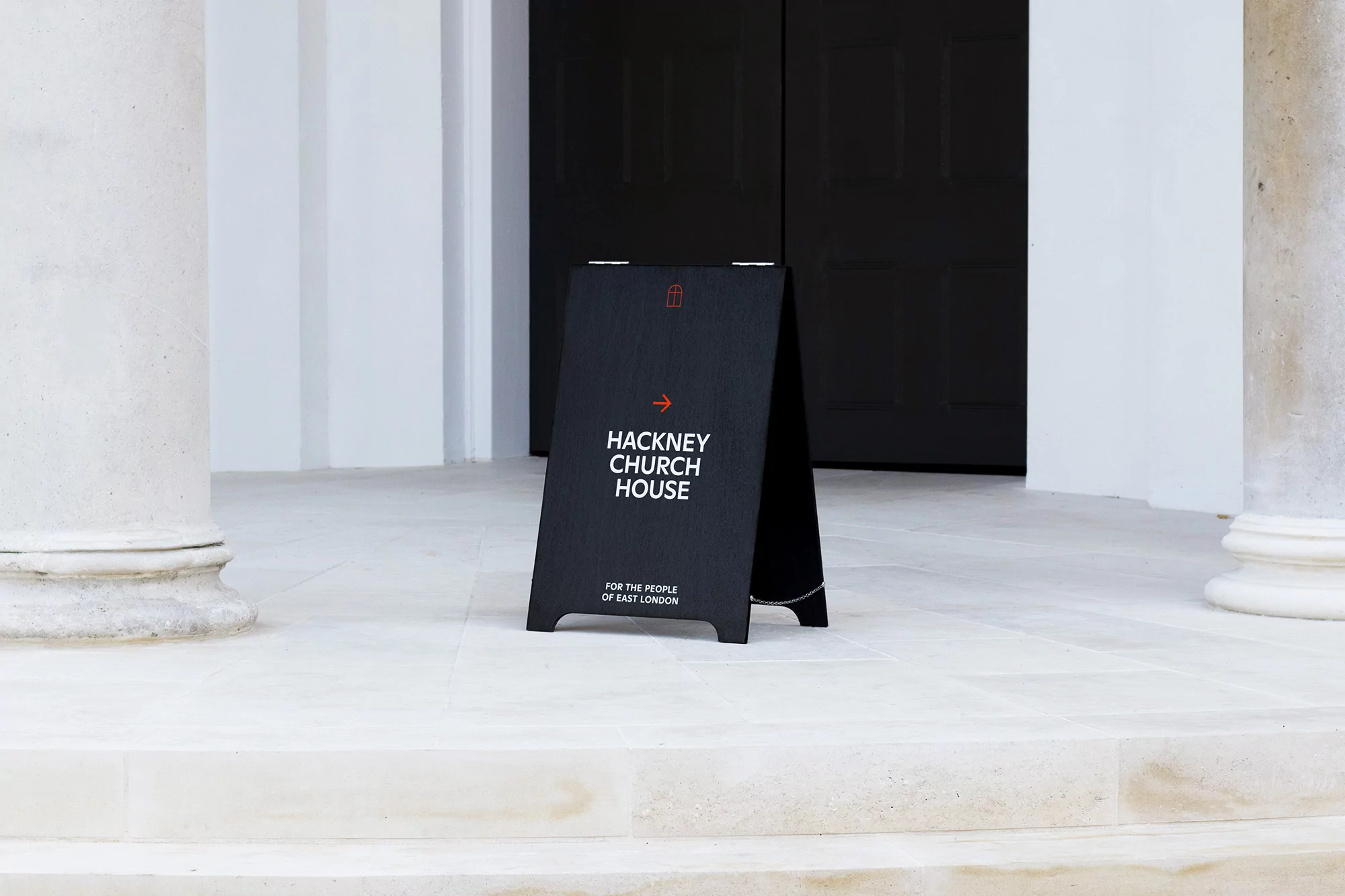 A-frame sign for Hackney Church House sits on stone steps between two pillars, directing people towards the entrance.
