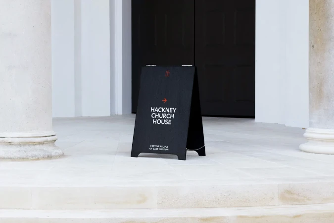 A-frame sign for Hackney Church House sits on stone steps between two pillars, directing people towards the entrance.