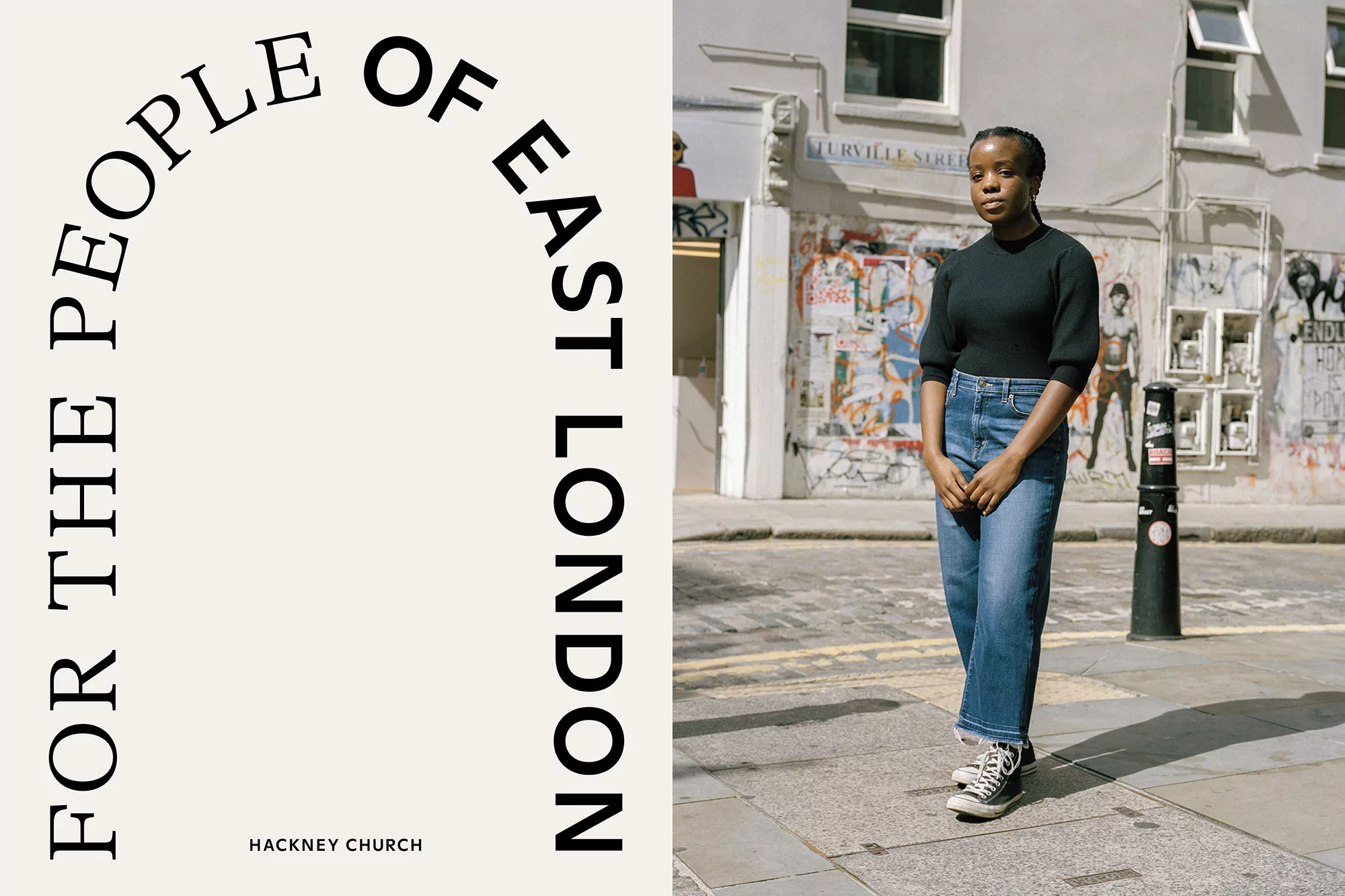Adult female in dark top and blue jeans stands on a city street with vintage buildings and a poster; lifestyle fashion photography.