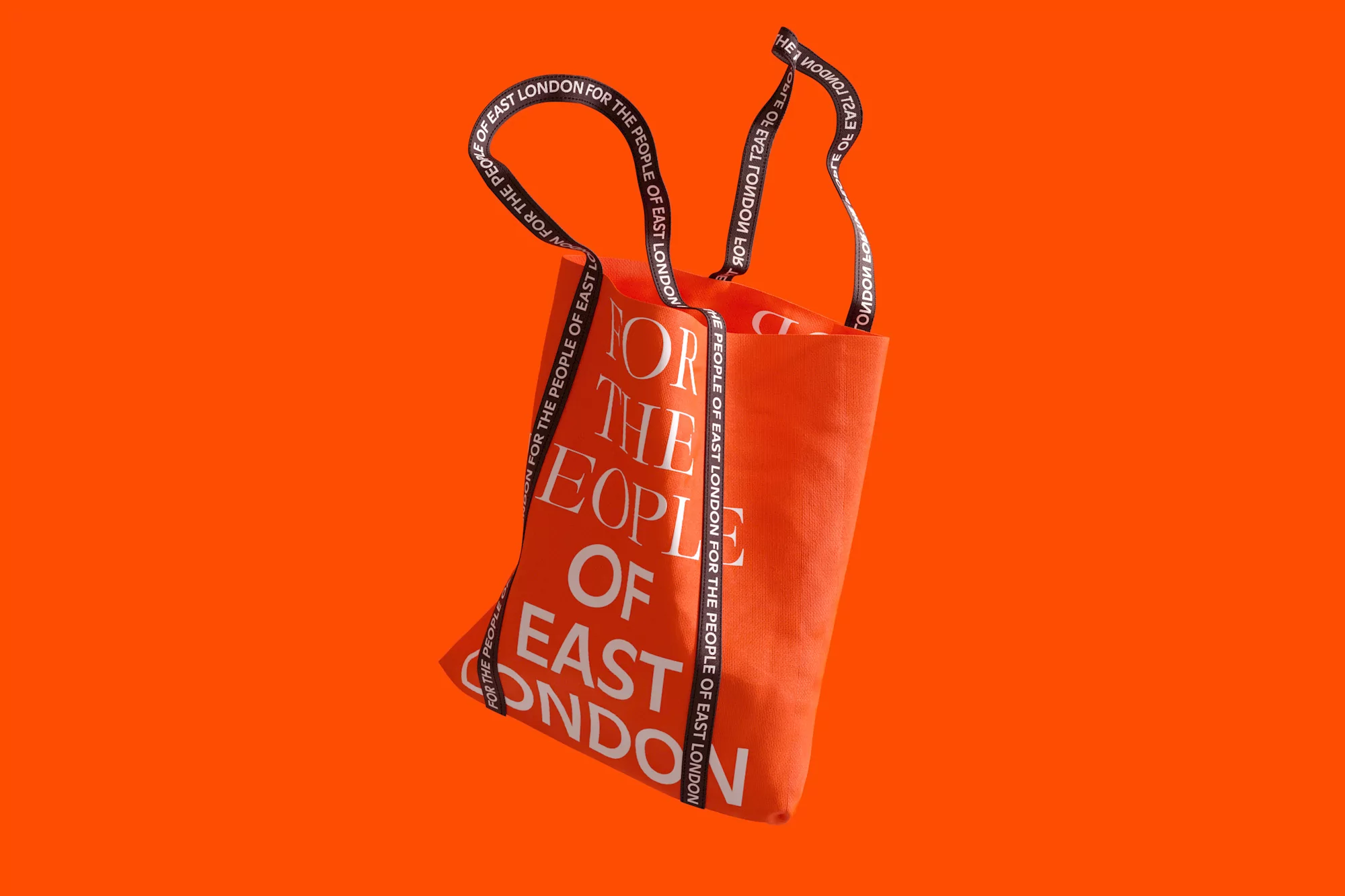 Eye-level shot of an orange tote bag with white text and black straps against an orange background, emphasizing minimalist design.