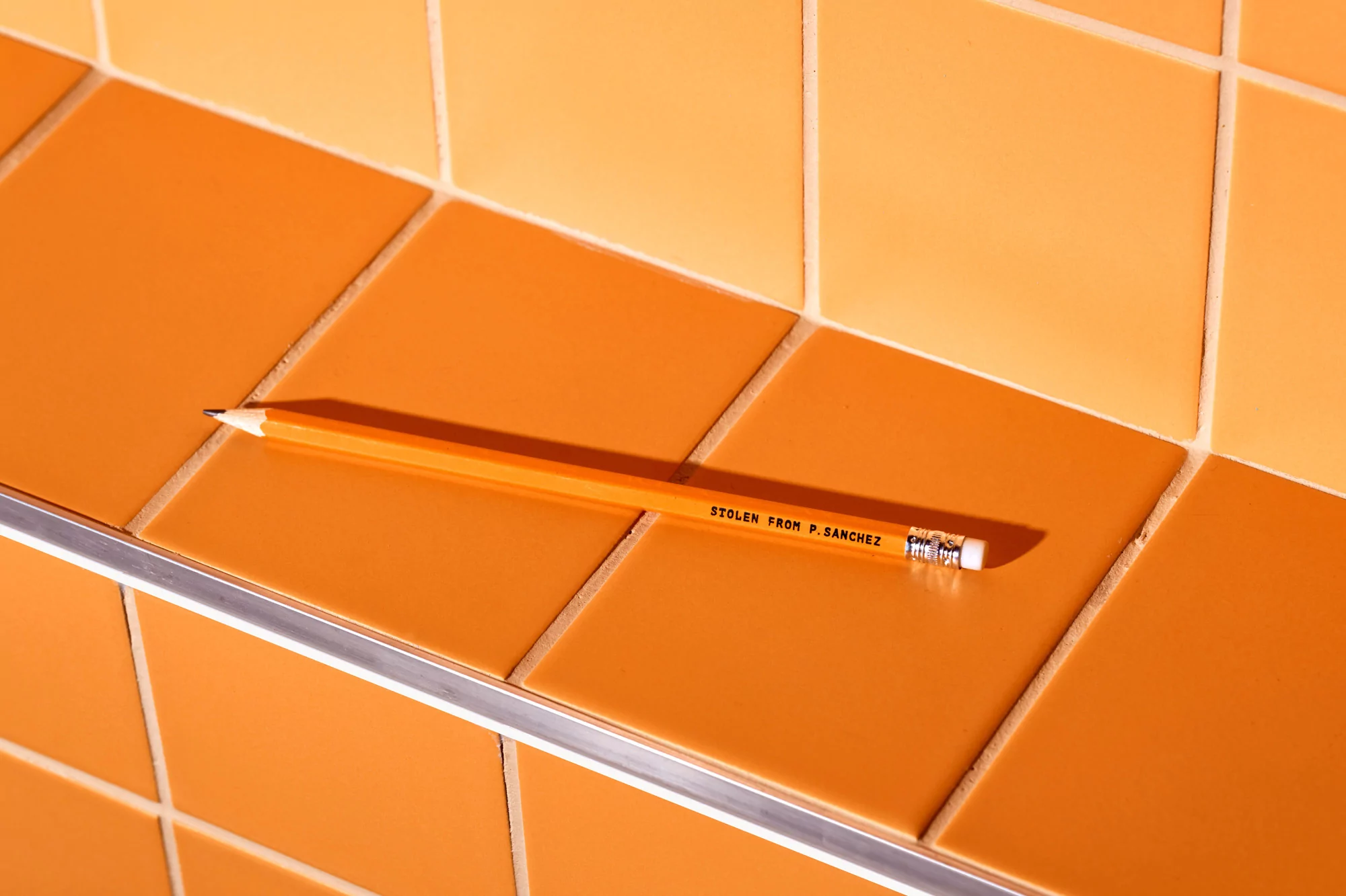 A yellow pencil with 'Stolen from P. Sanchez' on orange tiled surface. Close-up, highlighting texture and color contrast.