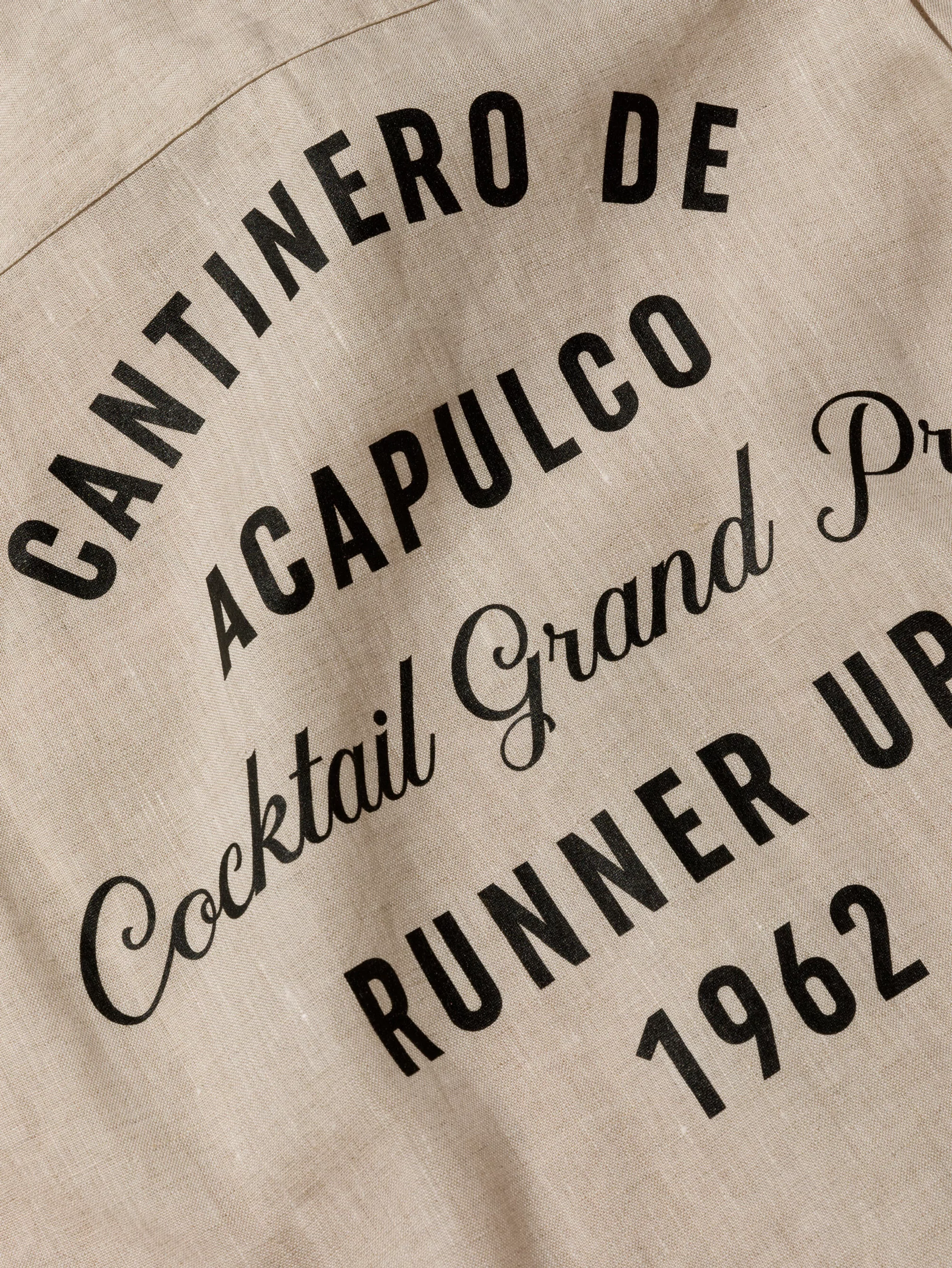 Text on beige fabric reads 'Cantinero de Acapulco Cocktail Grand Prix Runner Up 1962' in black serif and sans-serif fonts.