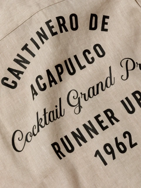 Text on beige fabric reads 'Cantinero de Acapulco Cocktail Grand Prix Runner Up 1962' in black serif and sans-serif fonts.