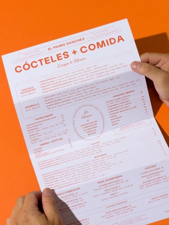 Hands holding a restaurant menu on a bright orange background. Menu features cocktails, food, and prices, with some text visible.