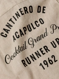 Close-up of beige linen fabric with black printed typography reading Cantinero de Acapulco Cocktail Grand Prix Runner Up 1962.