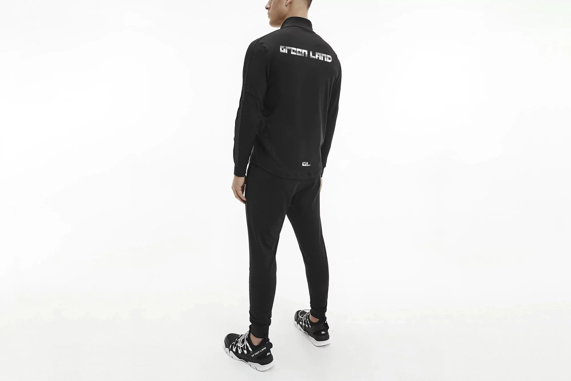 A person is seen from the back wearing a black jacket, black pants, and sneakers, all against a solid white studio backdrop.