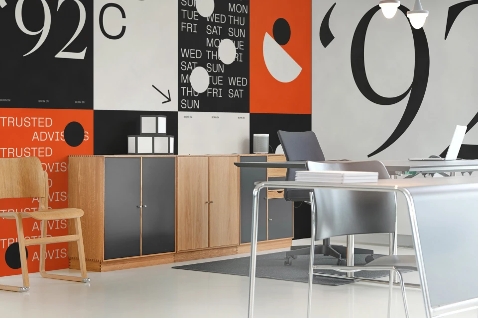 Minimalist office interior featuring modern furniture, a wooden chair, and geometric wallpaper with bold typography in orange, black, and white.