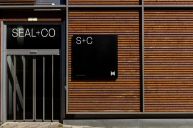 Modern building exterior with wooden slat paneling and black signage reading Seal+Co for corporate brand identity.