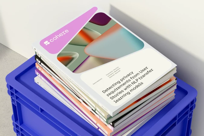 Stack of white paper documents from Cohere, featuring abstract geometric designs and company branding, resting on a blue plastic crate.