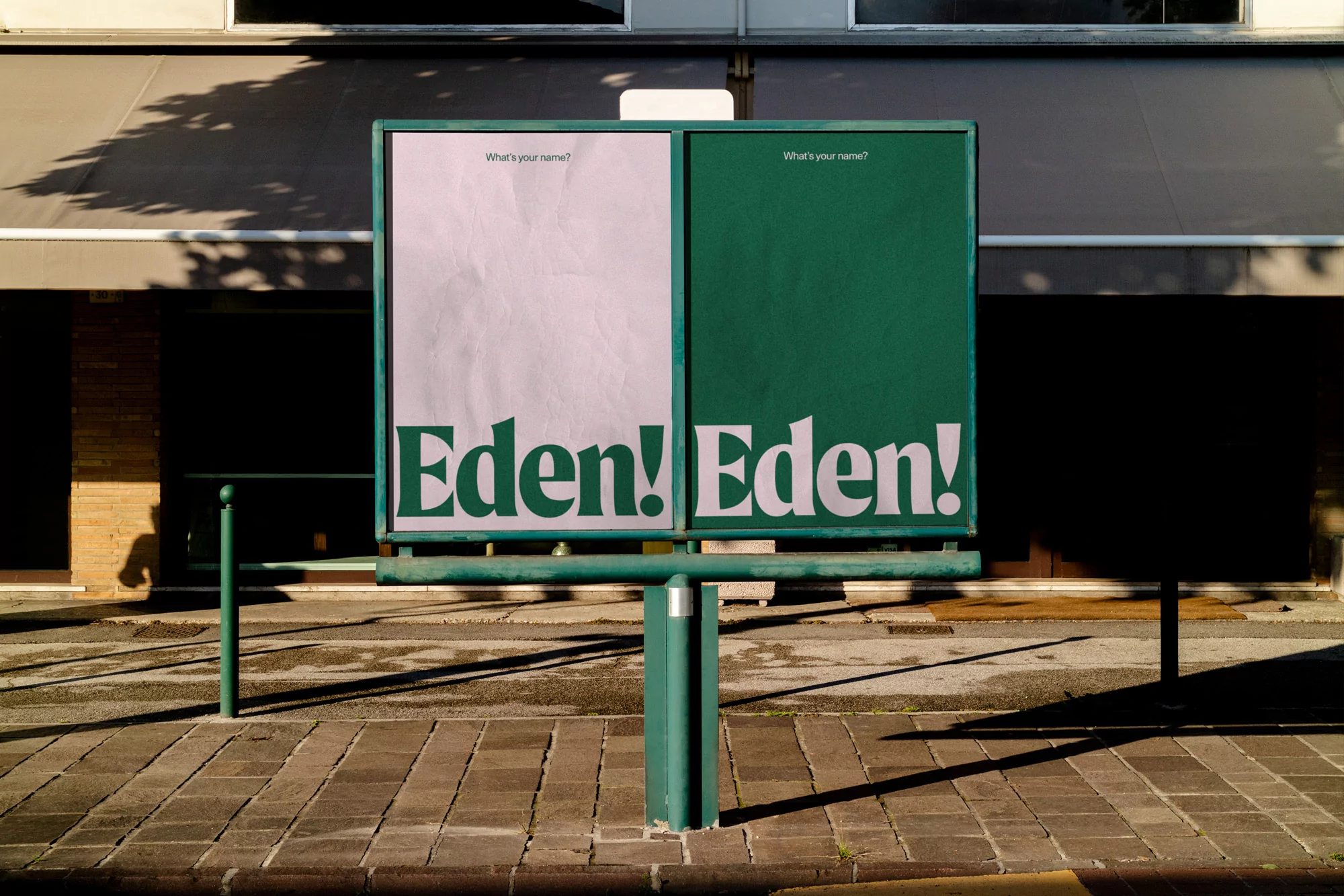 Outdoor advertisement billboard with 'Eden!' text on a brick sidewalk in front of a building with an awning, providing street-level advertising.