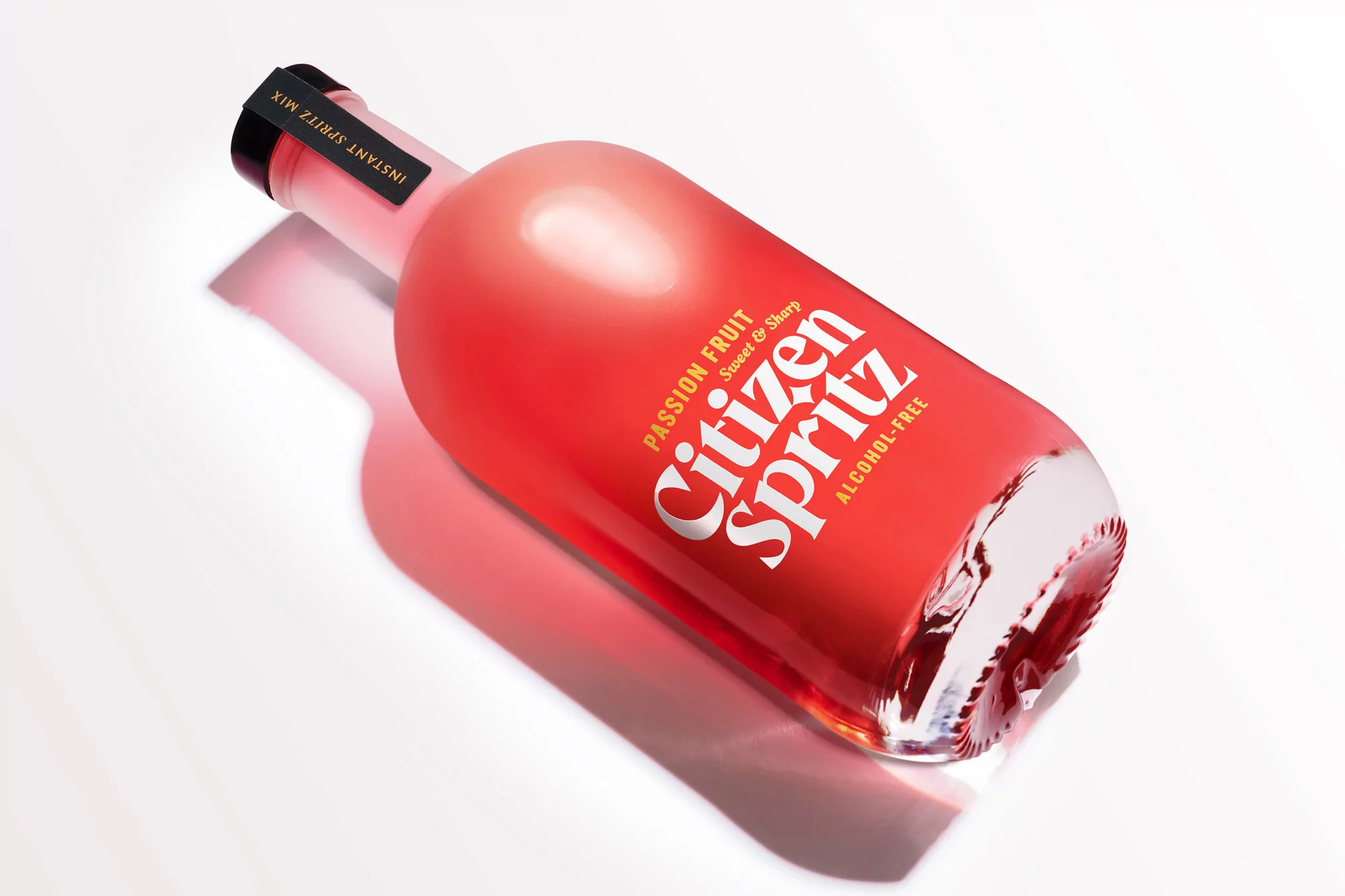 Eye-level studio shot of a red-tinted Citizen Spritz bottle with black cap on a white surface, showcasing the brand's modern aesthetic.