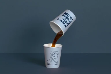 Prospect brand coffee cups on a grey background with coffee pouring from an upper tilted paper cup into a lower upright cup