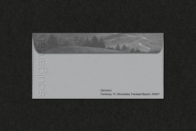 Grey envelope with an embossed brand name and landscape flap resting on dark textured paper