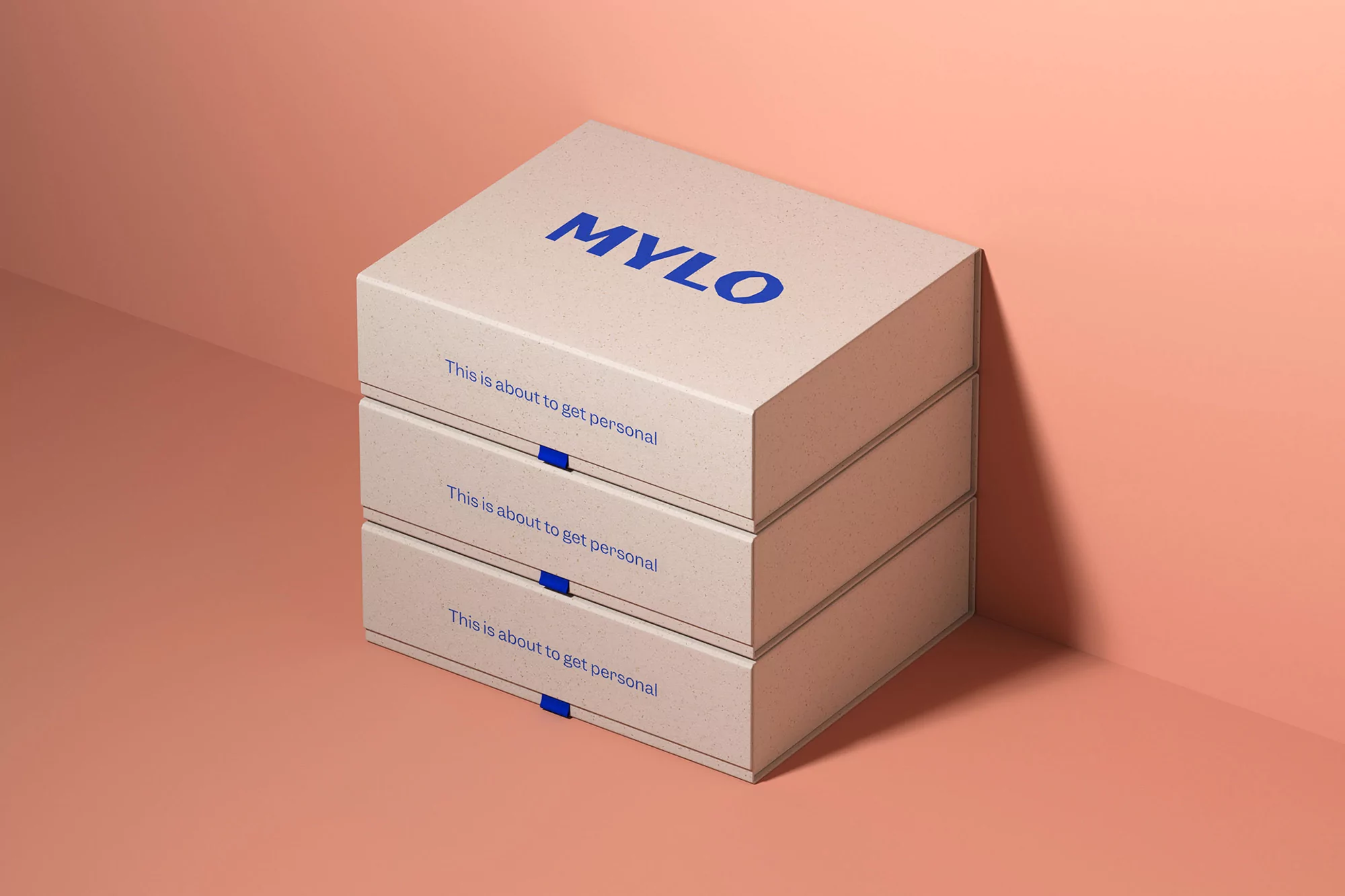 Stacked square boxes with 'MYLO' printed on top, in a studio setting with peach-colored background. Product presentation.