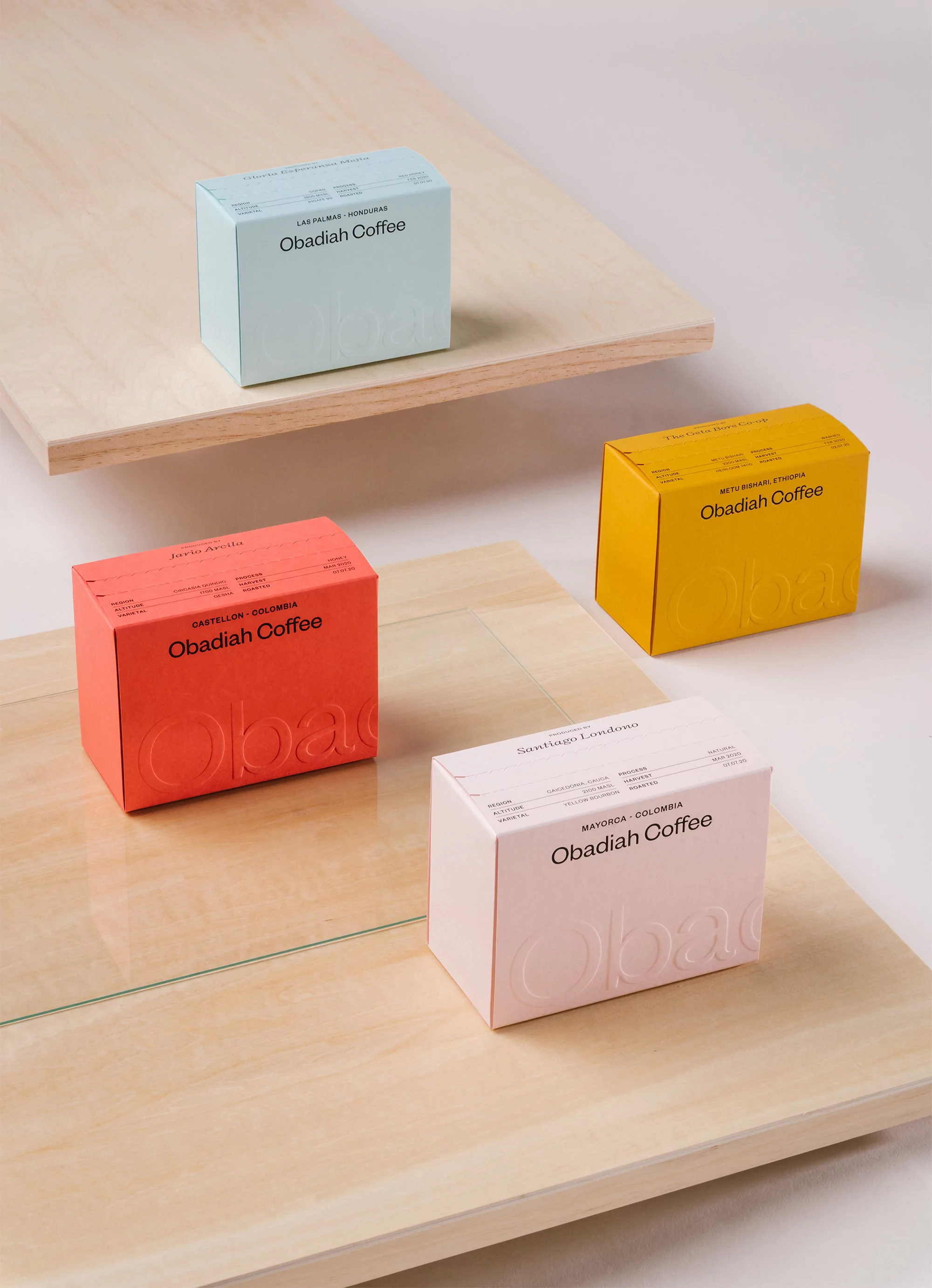 Four colorful Obadiah Coffee boxes on wooden platforms showcase product packaging in a minimalist, high-angle product shot.