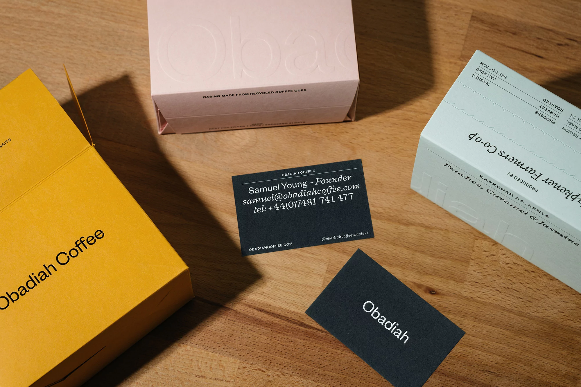 Close-up of Obadiah Coffee packaging on a wood surface, including product boxes and business cards displaying contact information.