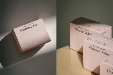 Split view of minimalist light pink Obadiah Coffee boxes with clean typography and debossed branding on smooth surfaces.