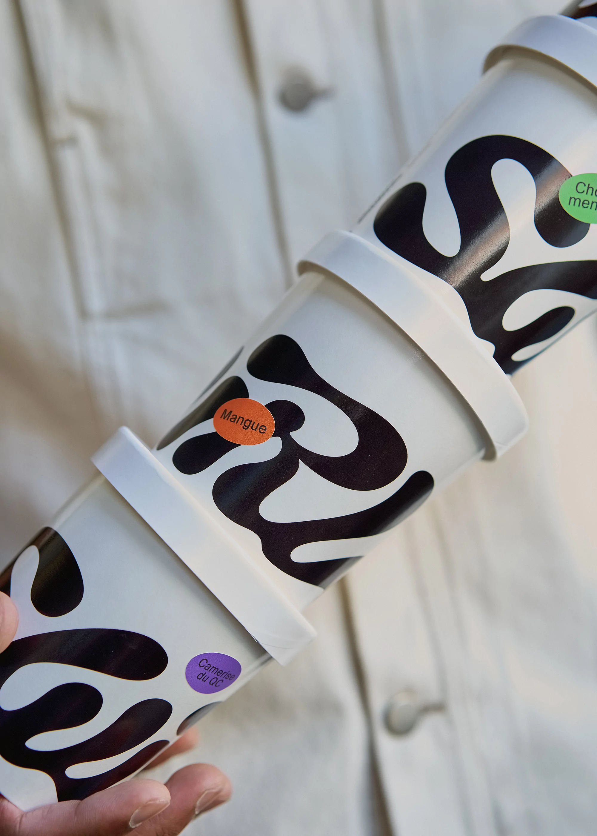 Close-up of a person holding a stack of three patterned ice cream containers with colorful flavor labels against a jacket backdrop.
