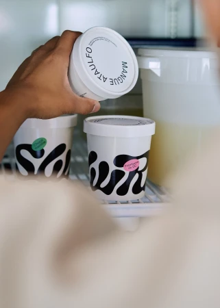 Hand reaches for white containers of mango sorbet in a refrigerator. Containers feature black wave designs and colorful labels.