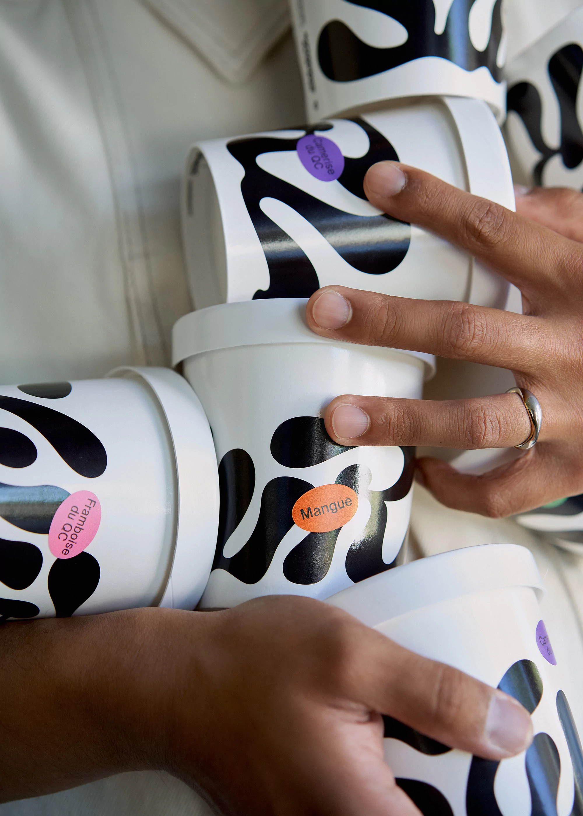 Close-up of stacked ice cream cups held by a person, featuring black and white patterned containers with fruit flavor labels.