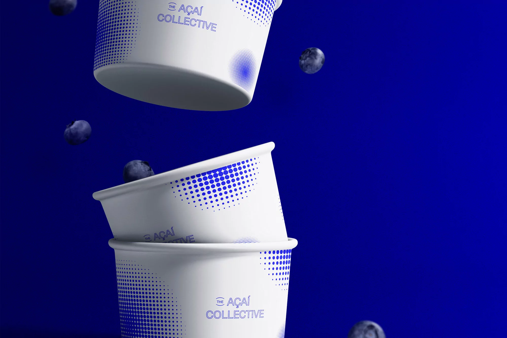 Three white paper cups decorated with blue dots and text stacked with scattered blueberries on a blue backdrop.