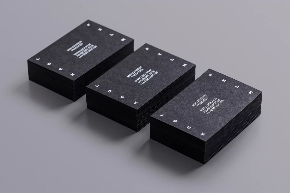 Three stacks of black business cards with white text and circular logo design elements arranged on a light gray surface.