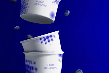 Three stacked white paper bowls with blue dotted branding patterns and falling blueberries against a solid deep blue background.