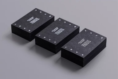 Three neat stacks of black business cards with white typography arranged diagonally on a smooth grey surface.