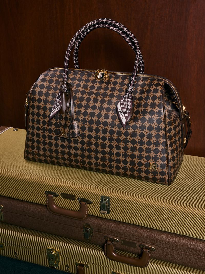 Patterned satchel handbag with scarf detail on stacked vintage suitcases, creating a still life fashion product shot.