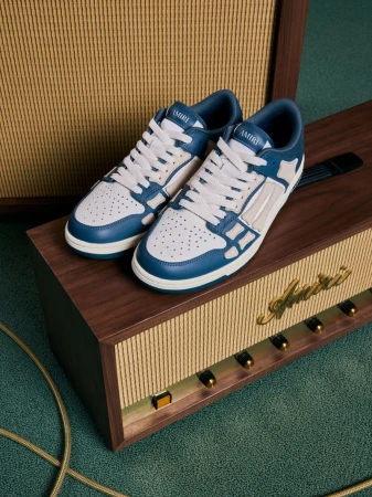 Amiri blue and white bone runner sneakers sit on top of a vintage wood and gold amplifier in a studio setting with green carpet.
