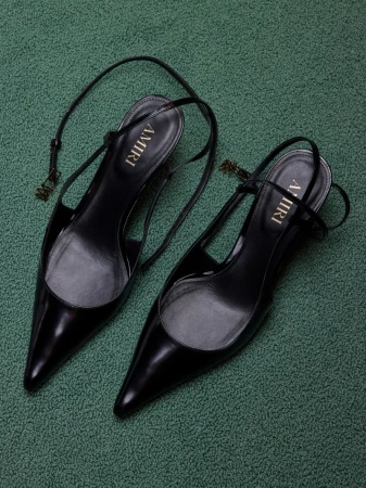 Pair of black AMIRI pointed-toe slingback high heels on a textured green surface, showcasing modern fashion footwear.