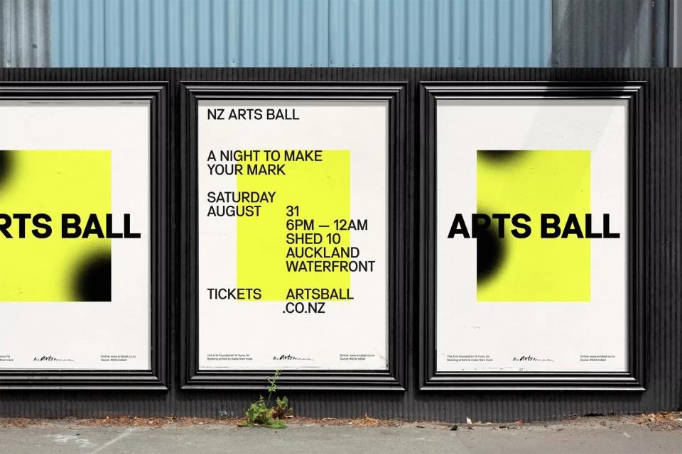 Three posters for the NZ Arts Ball feature a yellow square with a black gradient and bold text on a textured gray wall outdoors.