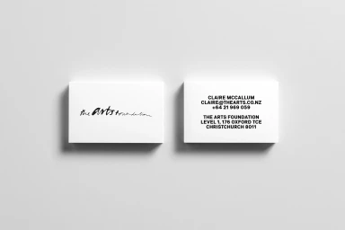 Two white business cards resting on a pale grey surface, showing a handwritten brand logo on one and contact details on the other.