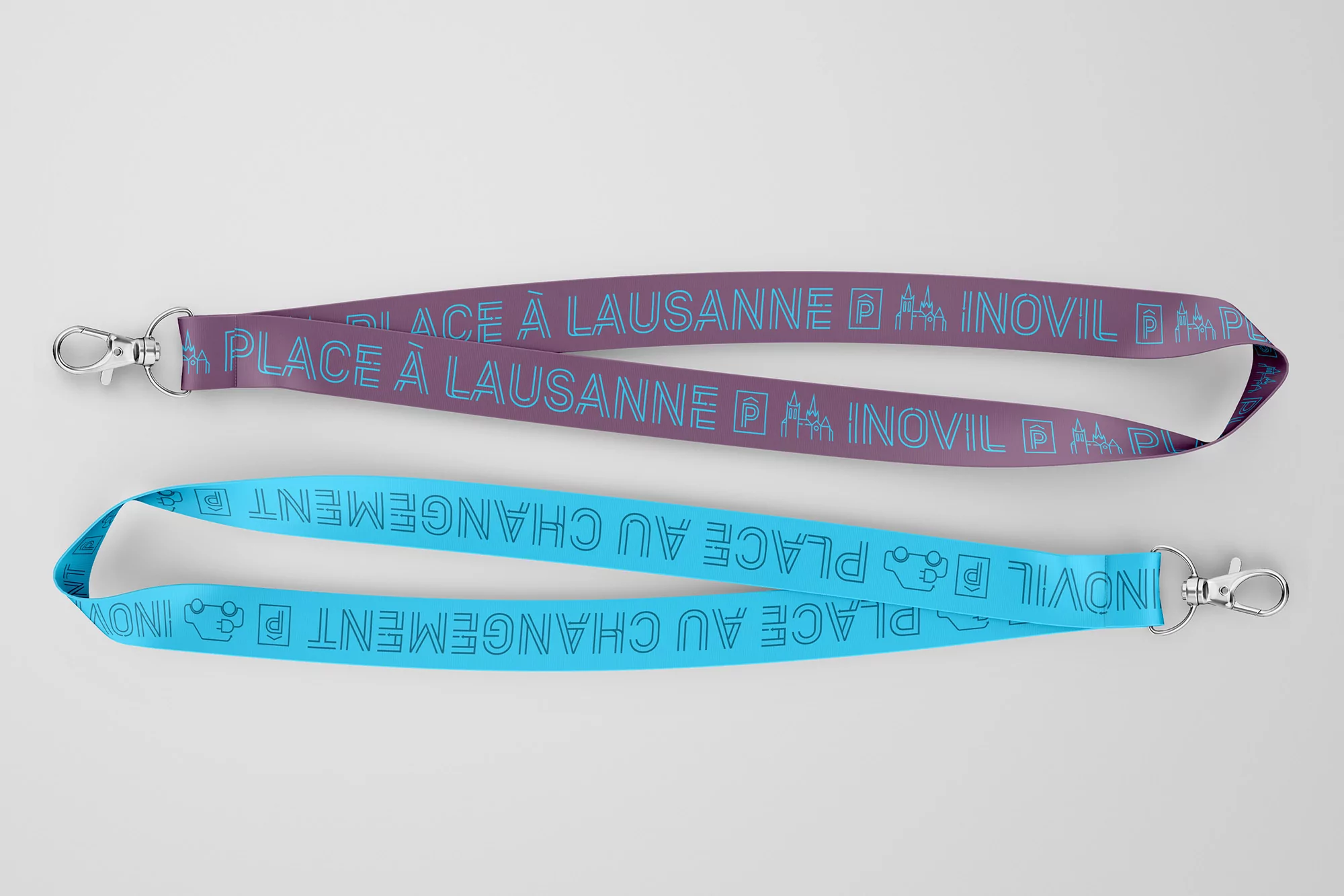 Two lanyards, one purple and one turquoise, with printed text and logos, arranged on a clean white background in a studio setting.