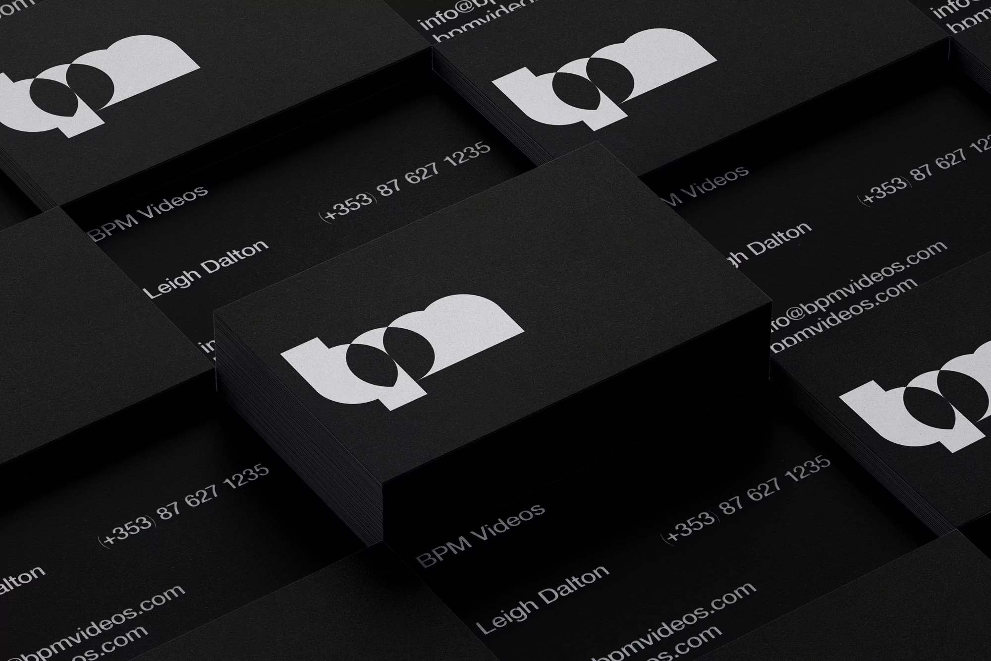 Stacks of black business cards with a white logo, contact details, and company name arranged in a geometric pattern.