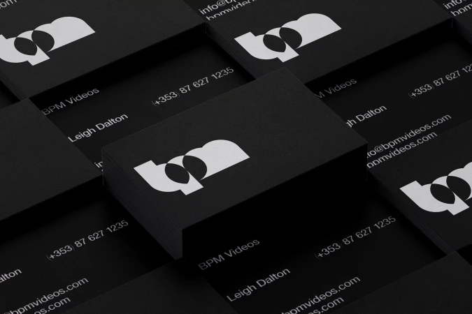 Stacks of black business cards with a white logo, contact details, and company name arranged in a geometric pattern.