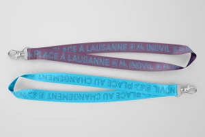 Two branded lanyards, one purple and one blue, featuring printed text and metal clasps displayed against a grey background.