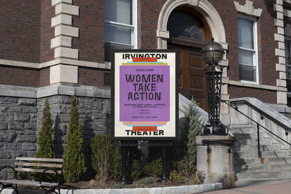 Outdoor view of a 'Women Take Action' event advertisement poster, in front of a brick theater building and stone steps on a sunny day.