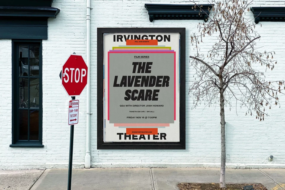Outdoor shot of a vintage movie poster for The Lavender Scare, mounted on a white brick wall with a stop sign and leafless tree.